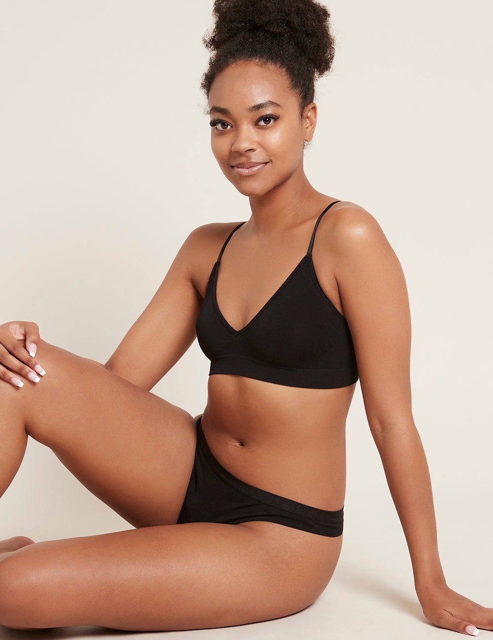 Person sitting casually, modeling comfortable black underwear set. Relaxed expression, showcasing a product in a shopping context