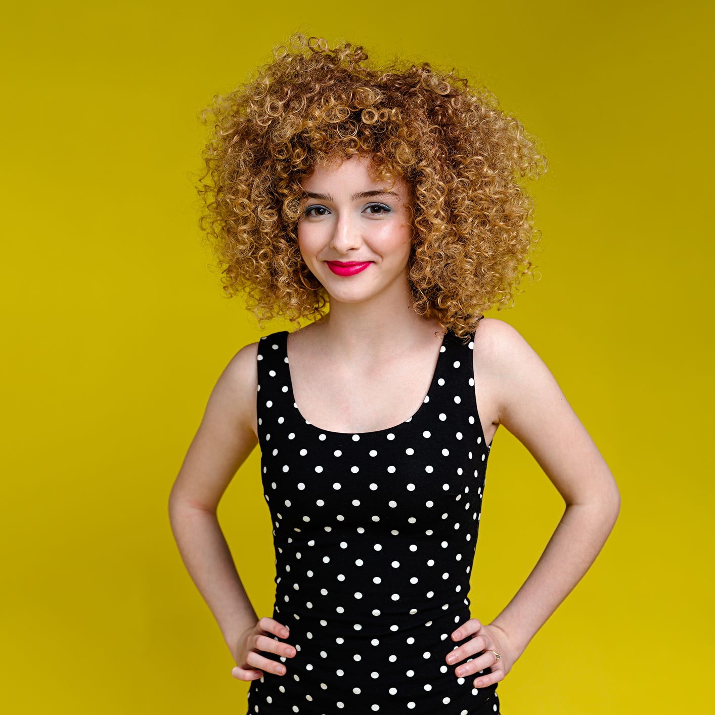 a portrait of a happy teenage girl wearing a polka dot dress standing in front of a yellow background