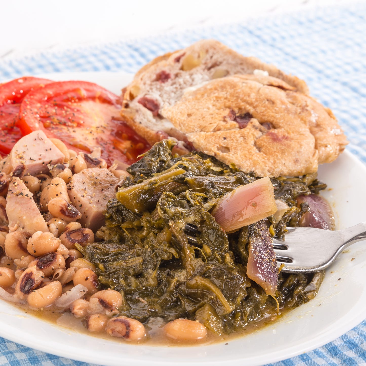 collard greens seasoned with salt pork and red onions and black eyed peas with chunks of spam  blue gingham tablecloth emphasizes country kitchen feel