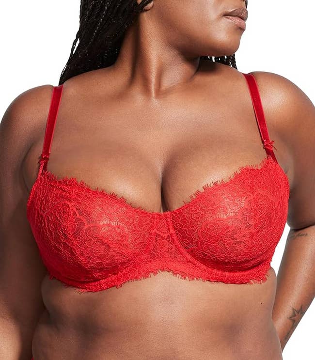 A person modeling a red lace bra with a confident pose