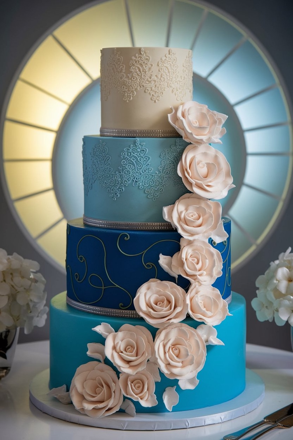 Royal Roses Elegance Cake – Ornate blue cake adorned with cream-colored roses and intricate designs.
