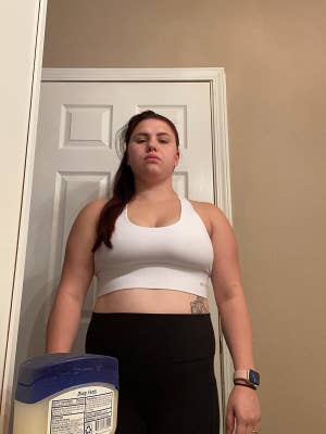 A reviewer stands in a room wearing a white sports bra and black leggings with a smartwatch