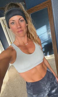 A reviewer takes a selfie in workout attire, wearing a sports bra and headband. She has a small smile and looks ready for a workout