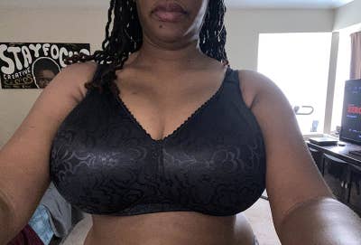 A person taking a selfie wearing a black patterned sports bra. In the background, there is a poster with partial text "STAY FOC..."