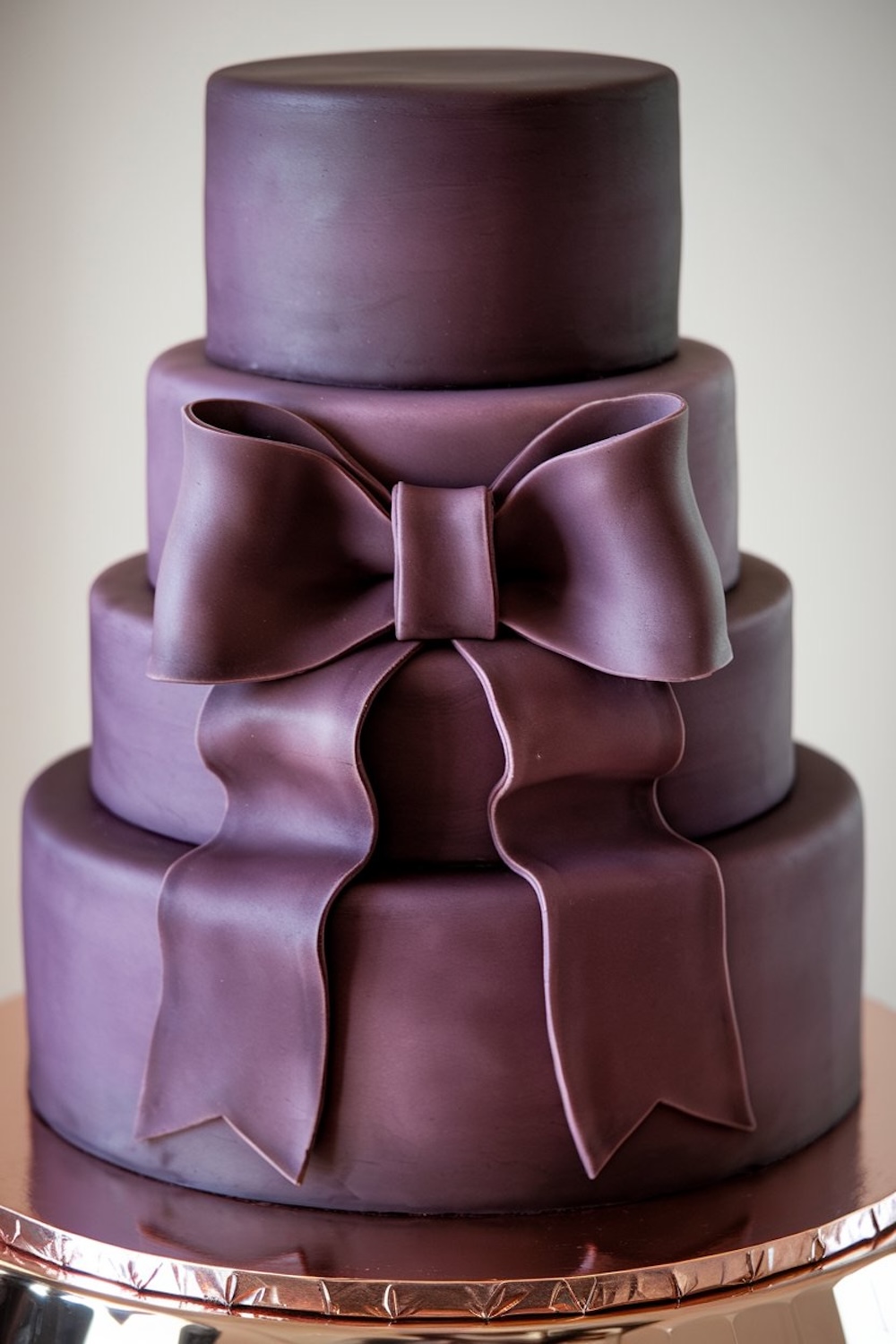 Three-tiered birthday cake with deep plum fondant and an oversized bow, showcasing an elegant purple cake aesthetic.