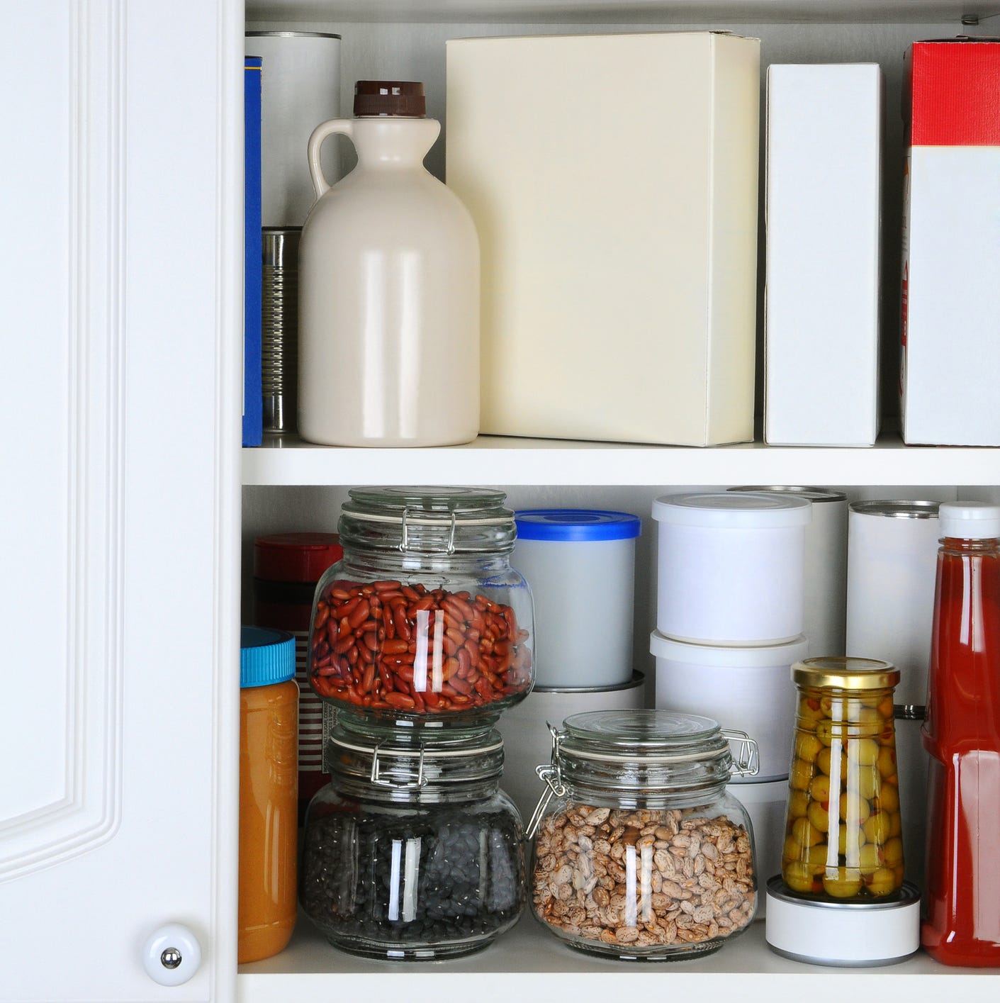 closeup of a well stocked pantry one door of the cabinet is open revealing canned goods, condiments, package foodstuffs, and storage jars