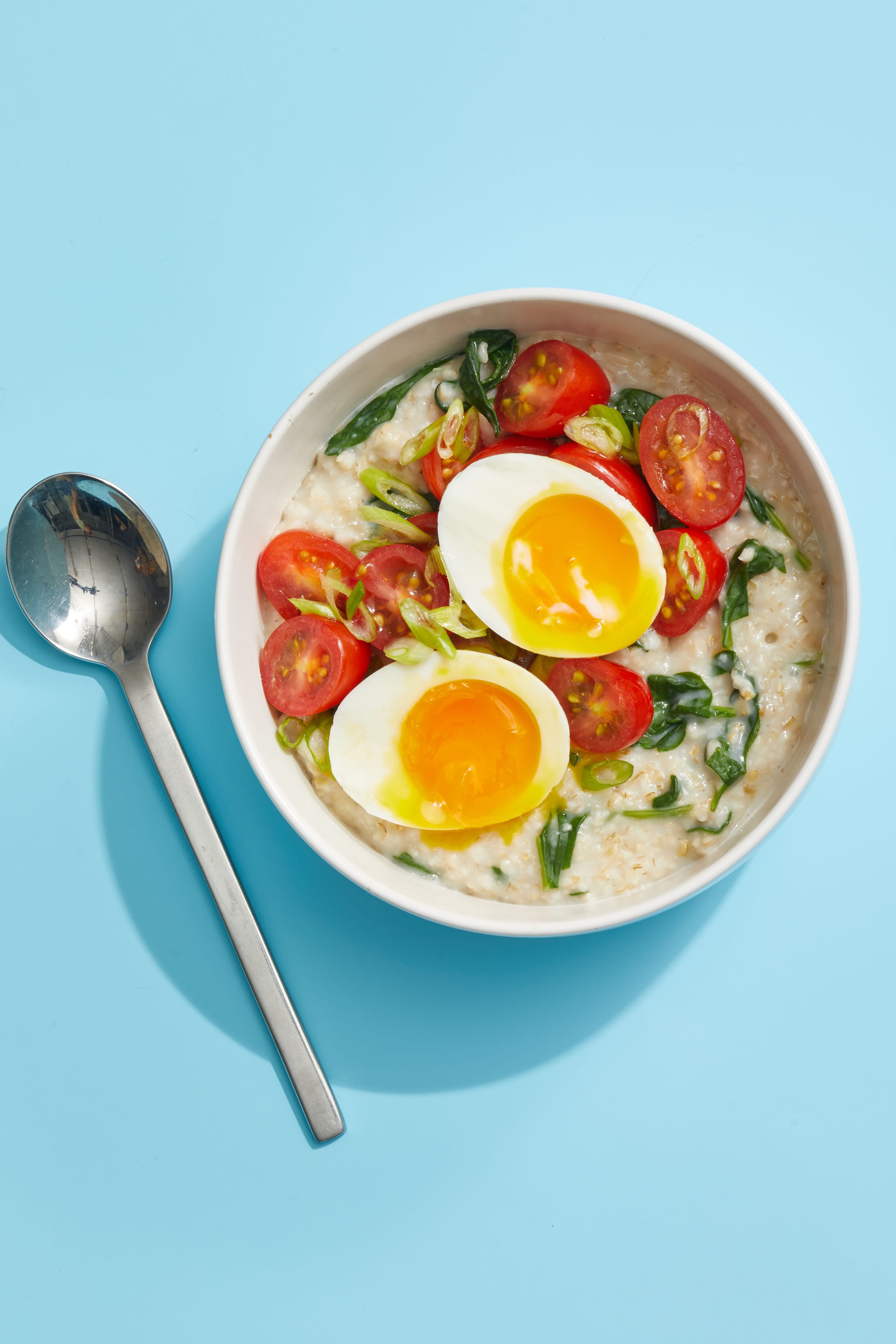 oatmeal with greens and eggs on blue background with spoon