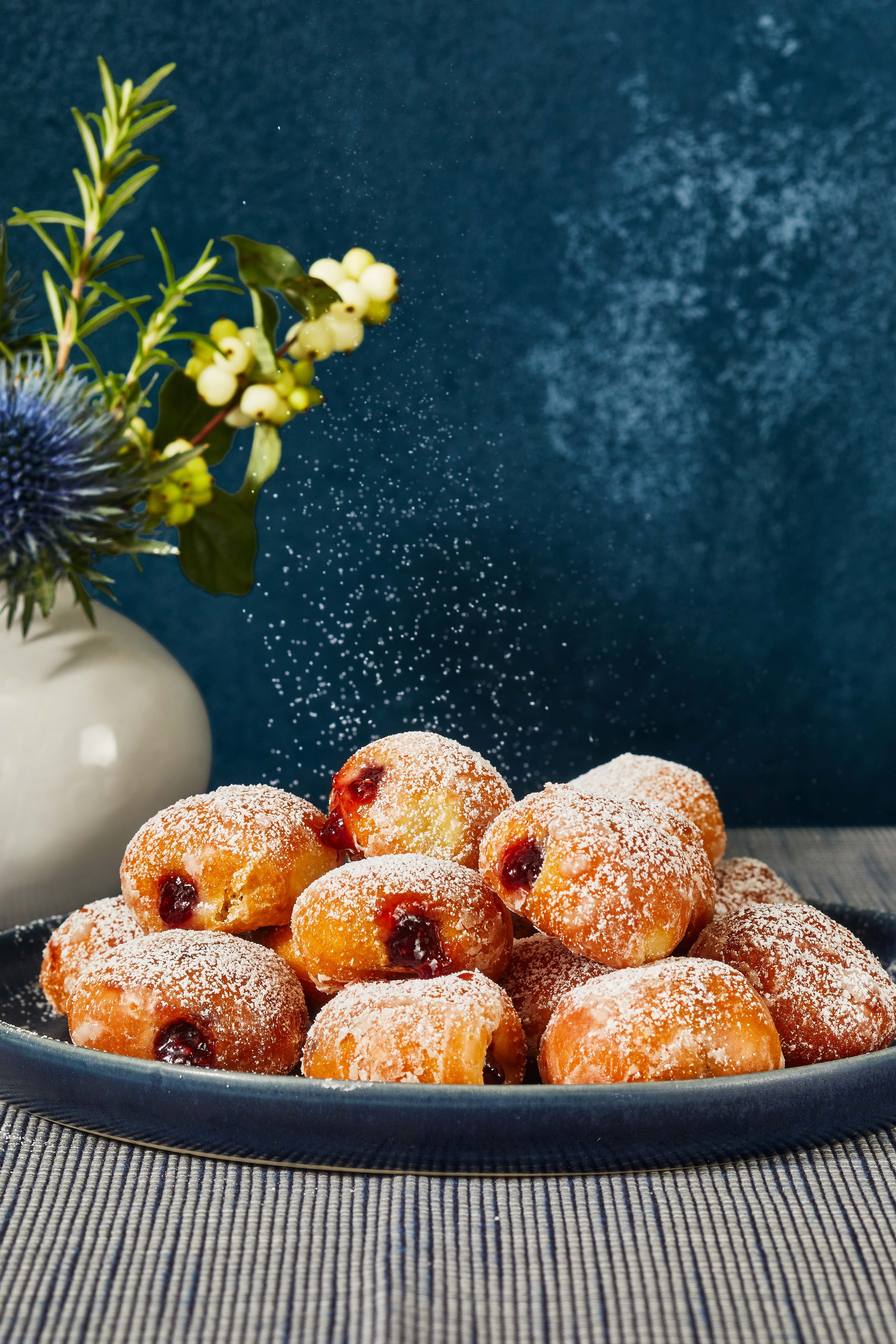 mini sufganiyot on a plate with confectioners' sugar sprinkled on top