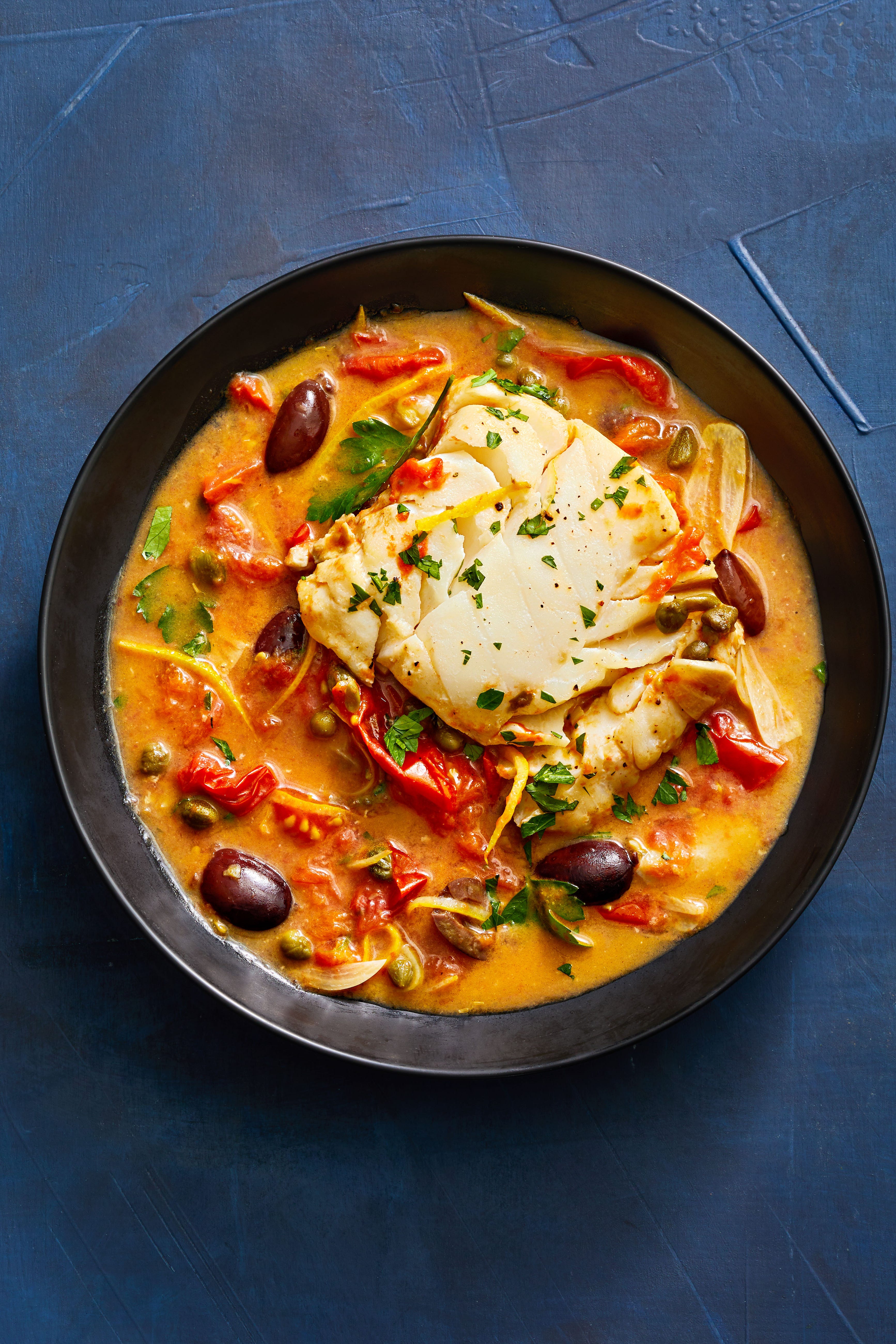 tomato poached cod with olives and capers in a black bowl