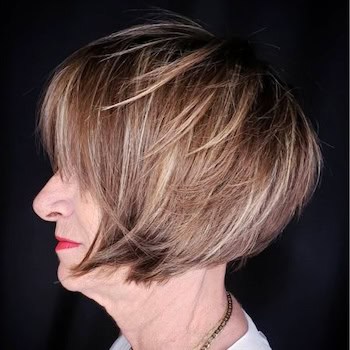 Choppy Layered Bob with Long Bangs hairstyle on a woman in her 60s with highlighted brown hair, side view.