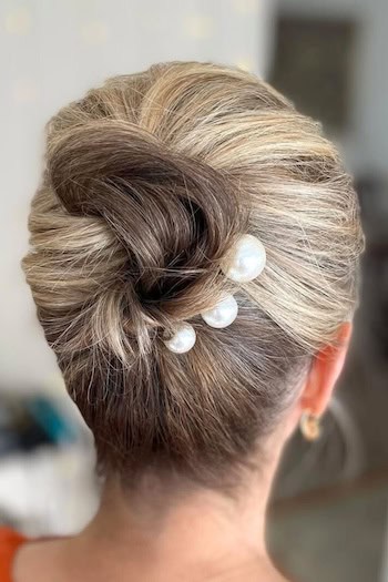 Elegant Twisted Updo with pearl details Hairstyle on an older woman with highlighted brown hair, side view.