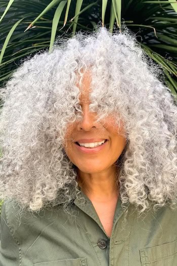 Voluminous Coils Hairstyle on a smiling older woman with silver hair.