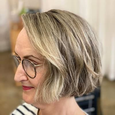 Textured Chin-Length Bob With Glasses Hairstyle on a smiling older woman with short blondish brown hair, side view.