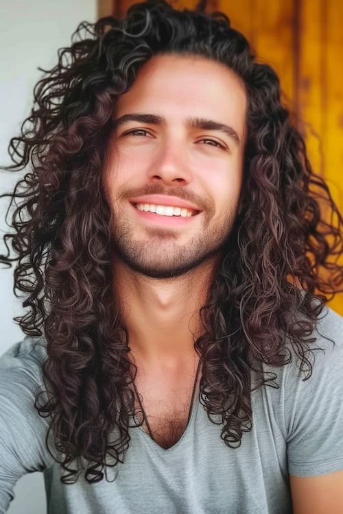 Curly ringlet long brown hairstyle on young man with beard.
