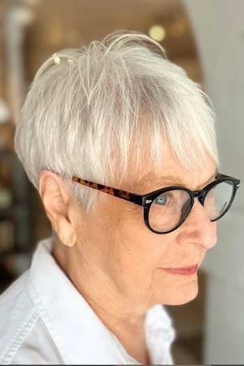 Straight Silver Pixie with Bangs Haircut on a woman in her 70s with glasses.