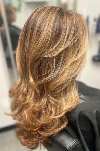 Layers With Soft Waves Hairstyle on an older woman with layered brown hair with blonde highlights, back view.