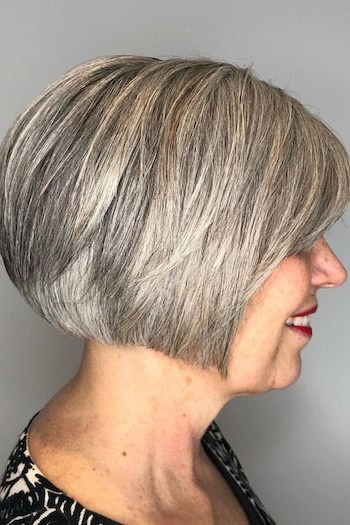 Short Bob With Subtle Layering Hairstyle on a smiling older woman with layered silvery gray hair, side view.