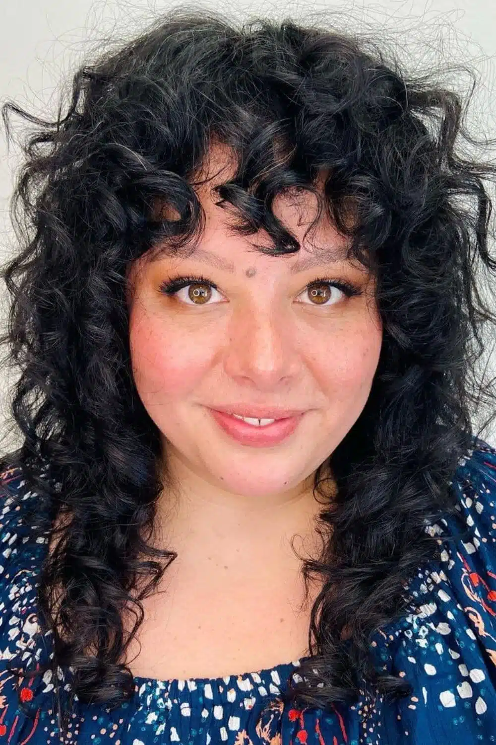 A woman with a medium-length black curly hair with curly bangs.