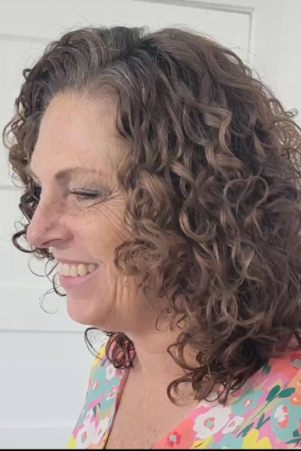 A woman with short brown layered curls with a deep side part.