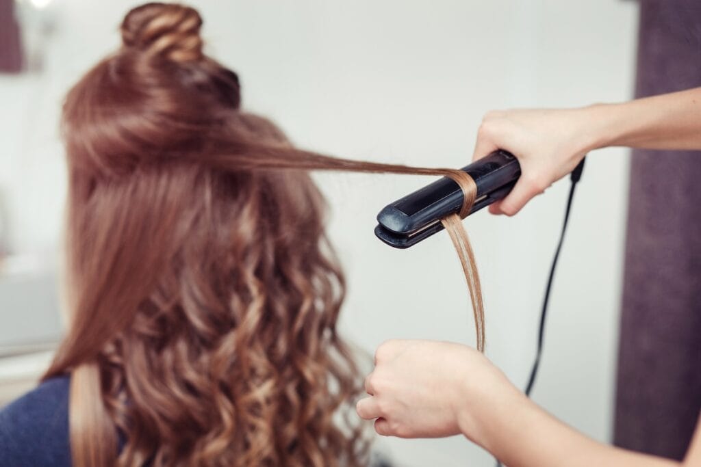 Hairstylist using flat iron on curly brown hair, from back.
