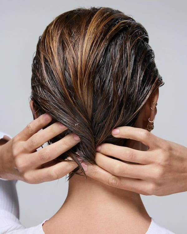 Woman with her hands touching short wet hair, from back.