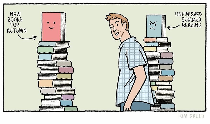 A man stands between two tall piles of books. On the left, a smiling stack labeled